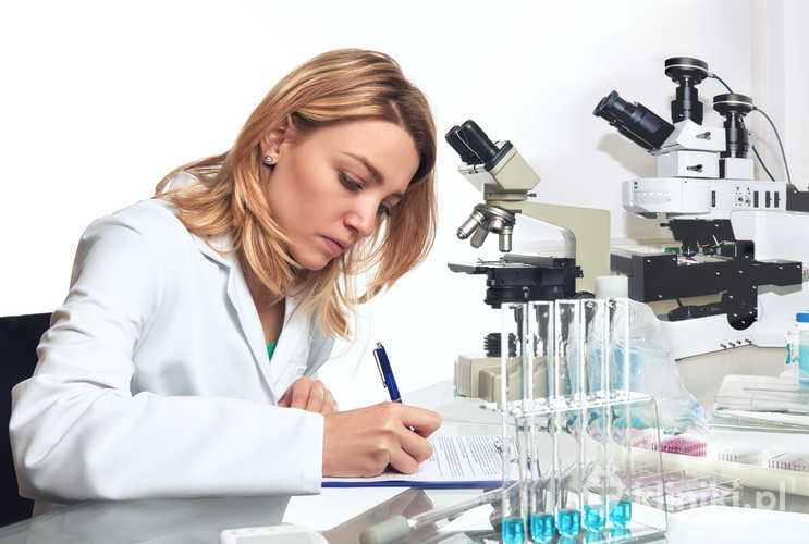 Młoda kobieta-naukowiec zapisuje wyniki obserwacji mikroskopowych w laboratorium badawczym