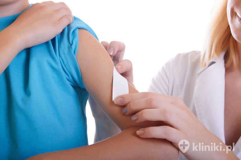 Lekarz ręką odrywa chłopcu plaster z ramienia Lekarz ręką odrywa chłopcu plaster z ramienia