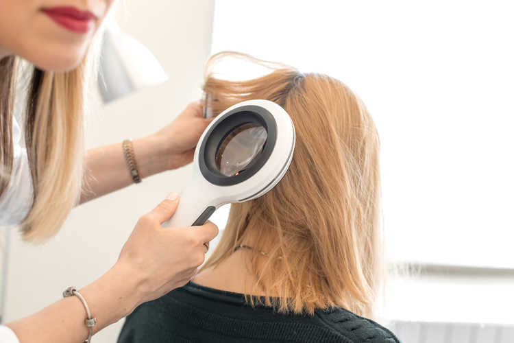 Trycholog bada stan włosów na głowie pacjenta za pomocą dermatoskopu