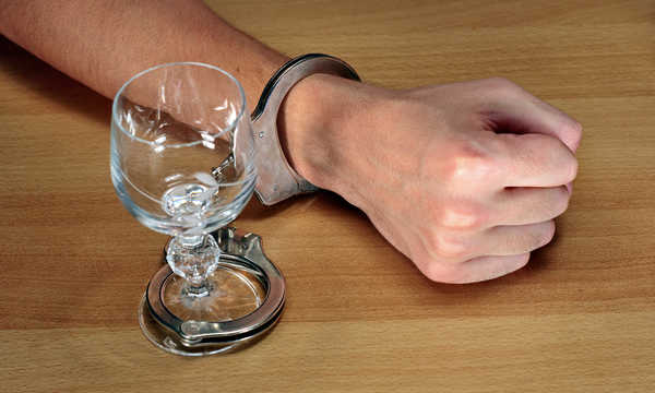 Uzależnienie od alkoholu, ręce skute kajdankami z pustą szklanką alkoholu