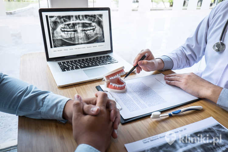 Profesjonalny dentysta pokazujący zdjęcie rentgenowskie szczęki i zębów oraz omawiający podczas konsultacji kwestie leczenia z pacjentem