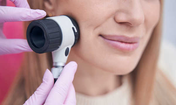 Dermatolog używający dermatoskopu podczas badania skóry pacjentki Dermatolog używający dermatoskopu podczas badania skóry pacjentki