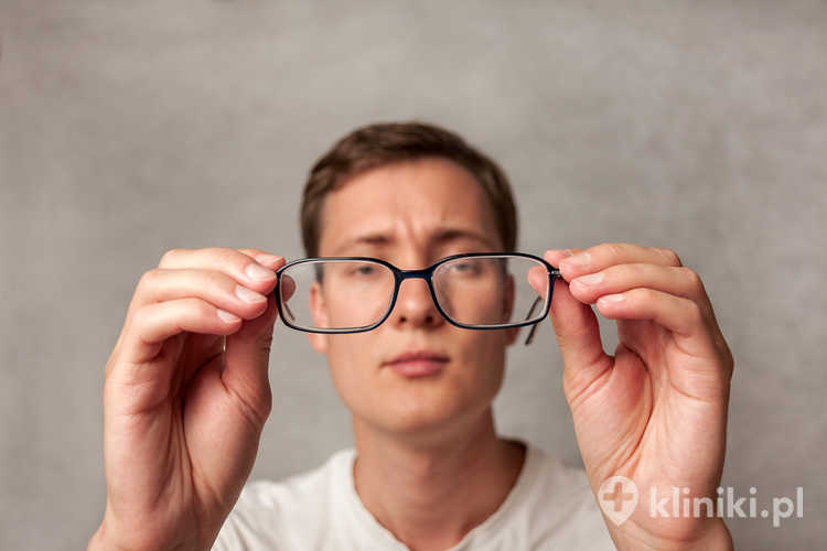 Młody mężczyzna trzyma okulary z soczewkami korekcyjnymi i patrzy przez nie