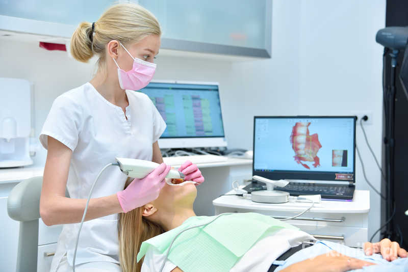Ortodonta skanuje pacjenta za pomocą wewnątrzustnego skanera stomatologicznego i nadzoruje proces na ekranie laptopa Ortodonta skanuje pacjenta za pomocą wewnątrzustnego skanera stomatologicznego i nadzoruje proces na ekranie laptopa