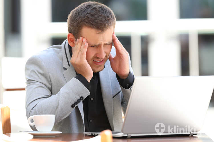 Zmęczony menadżer z bólem głowy pracuje online, siedząc w kawiarni